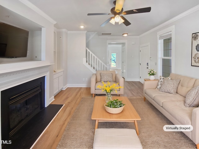 living room featuring light wood finished floors, visible vents, stairway, and ornamental molding