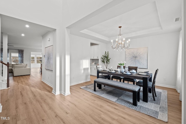 dining room with light wood-type flooring, a raised ceiling, visible vents, and baseboards