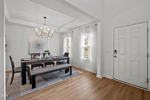 dining room with crown molding, a raised ceiling, an inviting chandelier, light wood-style floors, and baseboards