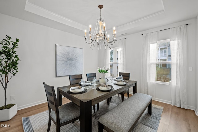 dining area featuring a raised ceiling, crown molding, baseboards, and wood finished floors