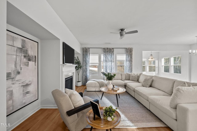 living area featuring baseboards, ceiling fan with notable chandelier, wood finished floors, and a glass covered fireplace