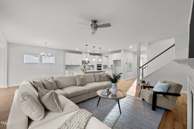 living area featuring recessed lighting, ceiling fan with notable chandelier, baseboards, stairway, and light wood finished floors