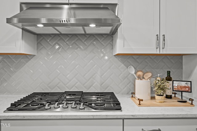 kitchen featuring decorative backsplash, light stone counters, ventilation hood, stainless steel gas stovetop, and white cabinetry