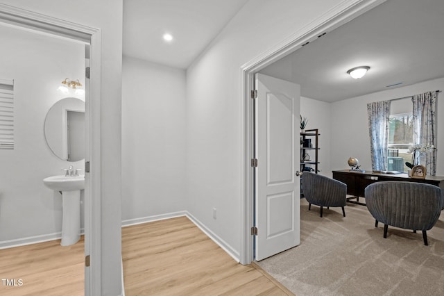 corridor featuring light wood finished floors, visible vents, baseboards, and a sink