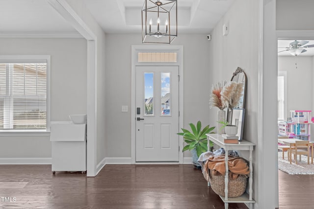 foyer entrance featuring ceiling fan with notable chandelier, a tray ceiling, baseboards, and wood finished floors