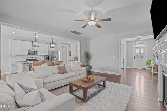 living room featuring baseboards, visible vents, hardwood / wood-style floors, and ceiling fan with notable chandelier