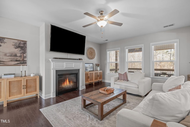 living area featuring a glass covered fireplace, dark wood finished floors, visible vents, and baseboards