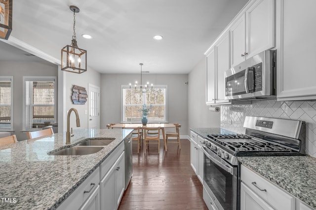 kitchen featuring stainless steel appliances, tasteful backsplash, an inviting chandelier, white cabinets, and a sink