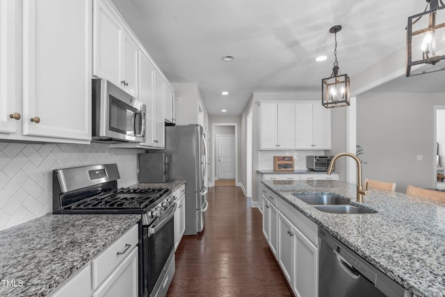 kitchen featuring stainless steel appliances, dark wood-type flooring, a sink, white cabinets, and pendant lighting