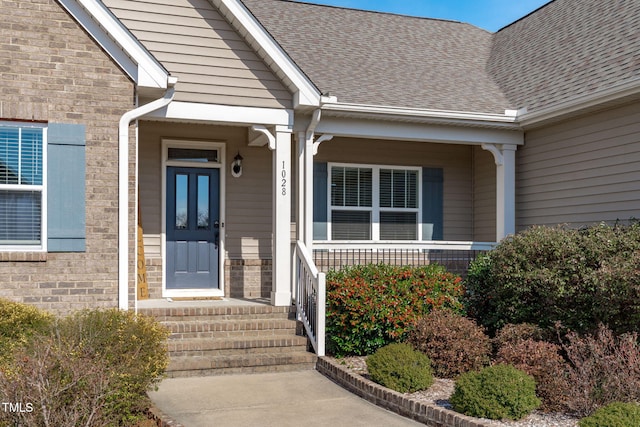 doorway to property with covered porch, brick siding, and a shingled roof