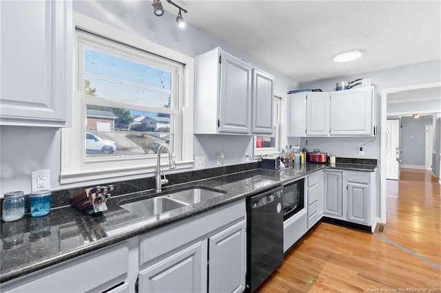 kitchen with light wood-style flooring, a sink, white cabinets, dark stone counters, and black appliances