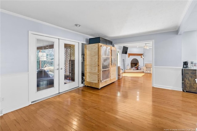 spare room with french doors, crown molding, ceiling fan, a lit fireplace, and hardwood / wood-style floors