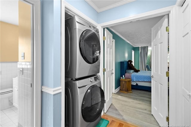 laundry area featuring a wainscoted wall, stacked washer and dryer, laundry area, wood finished floors, and ornamental molding