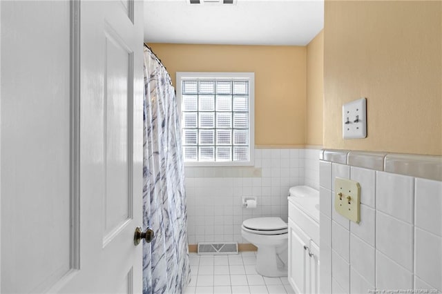 full bath with a wainscoted wall, tile walls, visible vents, toilet, and tile patterned flooring