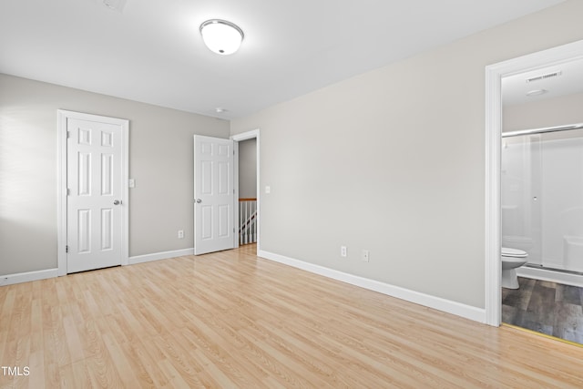 unfurnished bedroom featuring ensuite bathroom, wood finished floors, visible vents, and baseboards