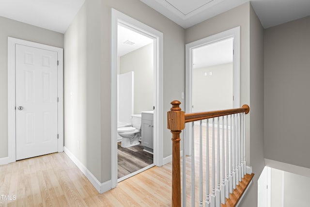 hallway with light wood-style floors, baseboards, visible vents, and an upstairs landing