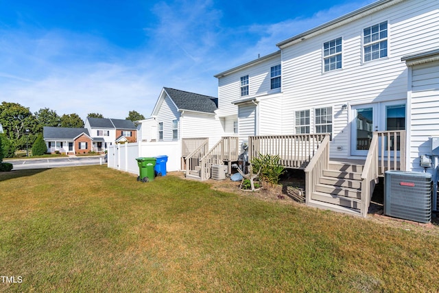 back of property with a deck, central AC unit, fence, a lawn, and a residential view