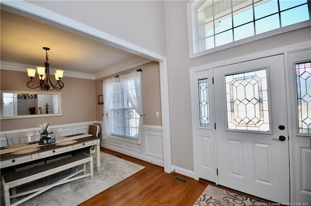 foyer featuring a notable chandelier, a decorative wall, a wainscoted wall, wood finished floors, and crown molding