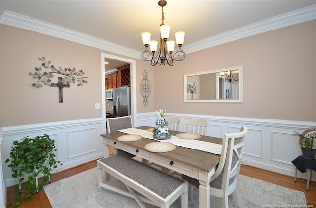 dining space featuring a wainscoted wall, crown molding, a notable chandelier, and wood finished floors