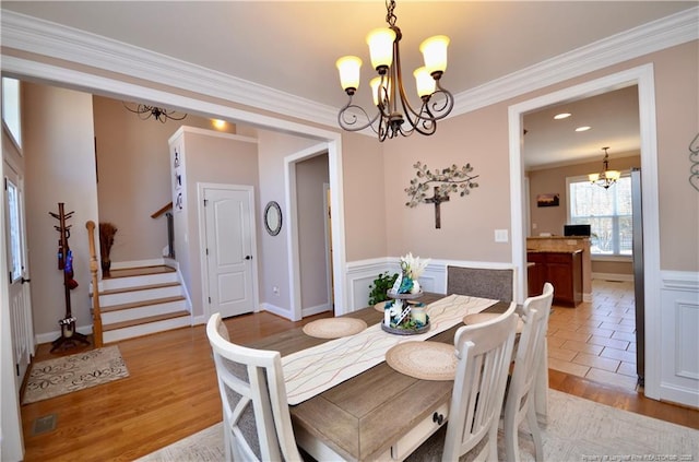 dining space with crown molding, light wood-style floors, stairway, and a notable chandelier