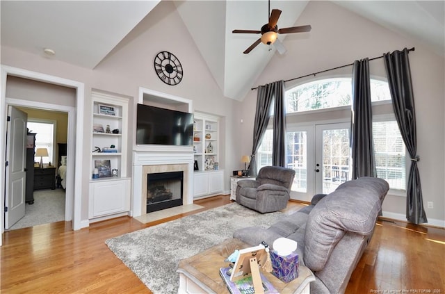 living room featuring a tile fireplace, french doors, a healthy amount of sunlight, and light wood-style flooring