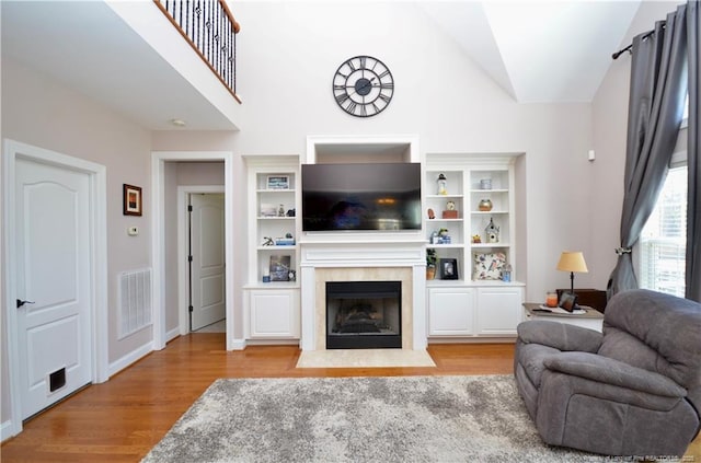 living room featuring high vaulted ceiling, a fireplace with flush hearth, wood finished floors, visible vents, and baseboards