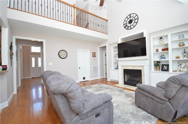 living area with baseboards, visible vents, wood finished floors, a high ceiling, and a high end fireplace