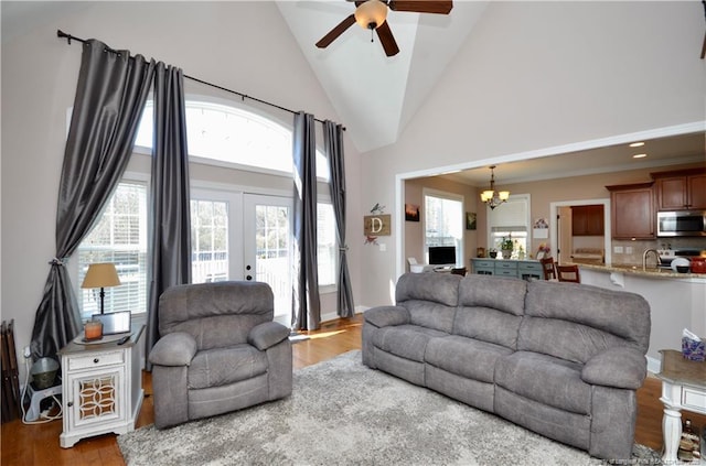 living area featuring high vaulted ceiling, ceiling fan with notable chandelier, french doors, and wood finished floors