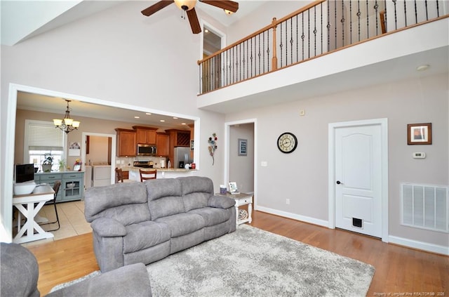 living room with light wood-type flooring, baseboards, visible vents, and ceiling fan with notable chandelier