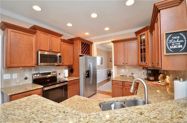 kitchen featuring brown cabinetry, wainscoting, light stone countertops, stainless steel appliances, and a sink