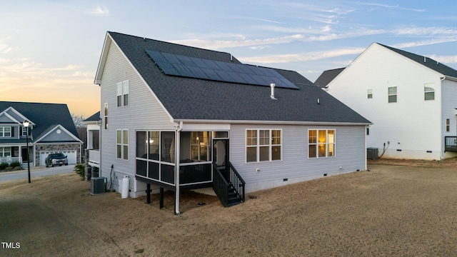 back of house at dusk featuring a sunroom, roof with shingles, crawl space, cooling unit, and roof mounted solar panels