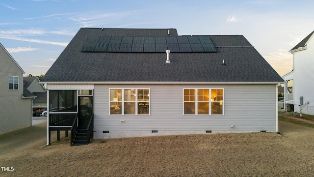 rear view of property with a shingled roof, crawl space, a sunroom, and solar panels