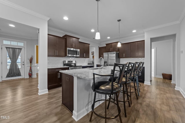 kitchen featuring stainless steel appliances, wood finished floors, a sink, an island with sink, and dark brown cabinets