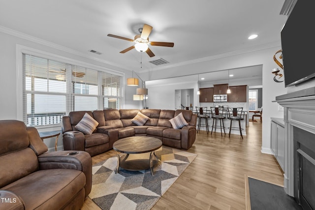 living area with light wood-style flooring, visible vents, and ornamental molding