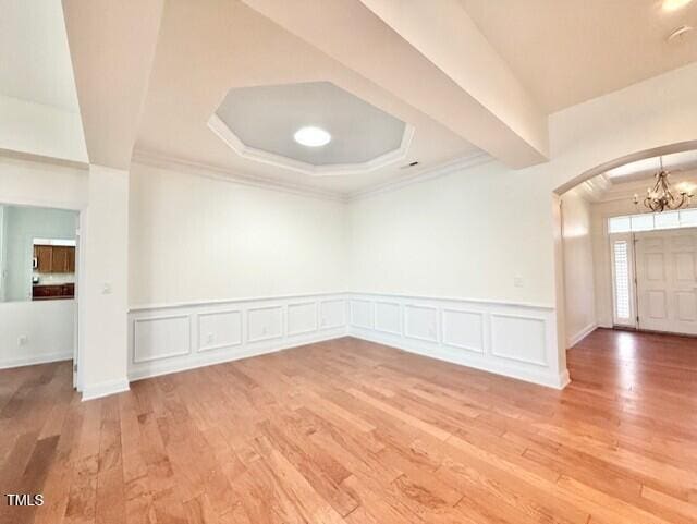 empty room featuring a notable chandelier, light wood-style flooring, a decorative wall, and ornamental molding