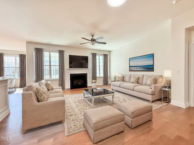 living area featuring a fireplace, baseboards, light wood-style floors, and a ceiling fan