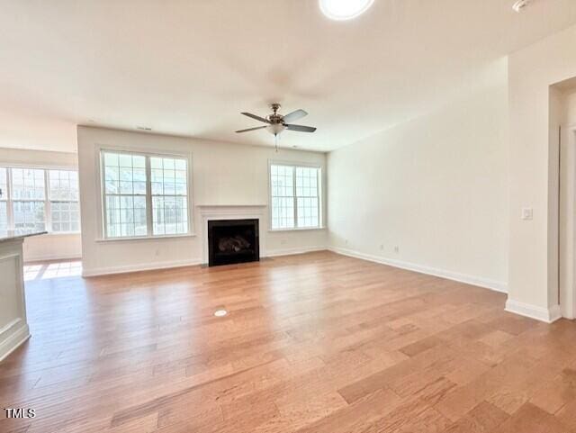 unfurnished living room featuring baseboards, a fireplace with flush hearth, light wood-style floors, and ceiling fan