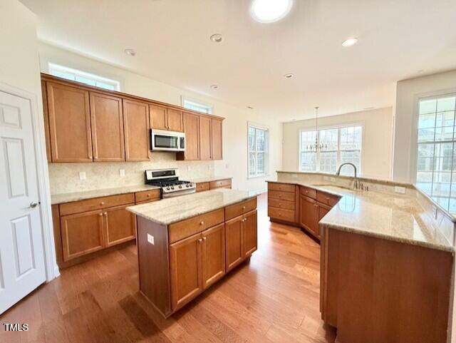 kitchen featuring a sink, stainless steel microwave, a spacious island, gas stove, and light wood finished floors