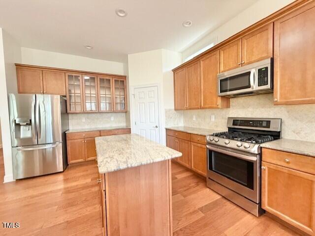 kitchen featuring light stone countertops, light wood-style flooring, decorative backsplash, appliances with stainless steel finishes, and a center island