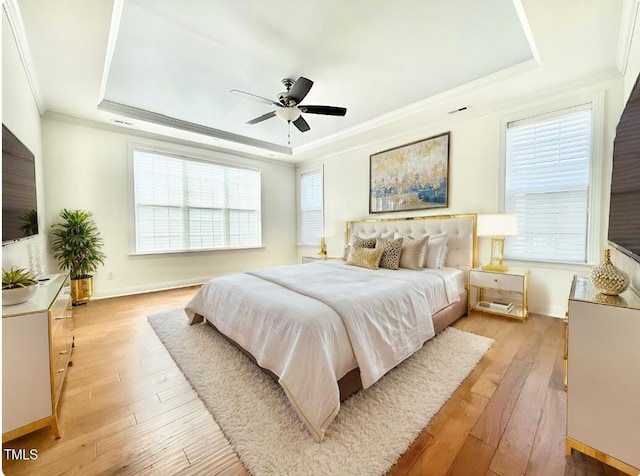 bedroom with light wood finished floors, multiple windows, and a raised ceiling