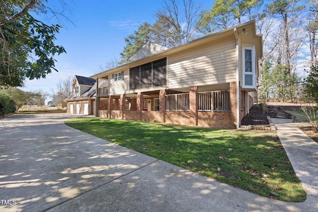 exterior space featuring a sunroom, concrete driveway, brick siding, and a front lawn