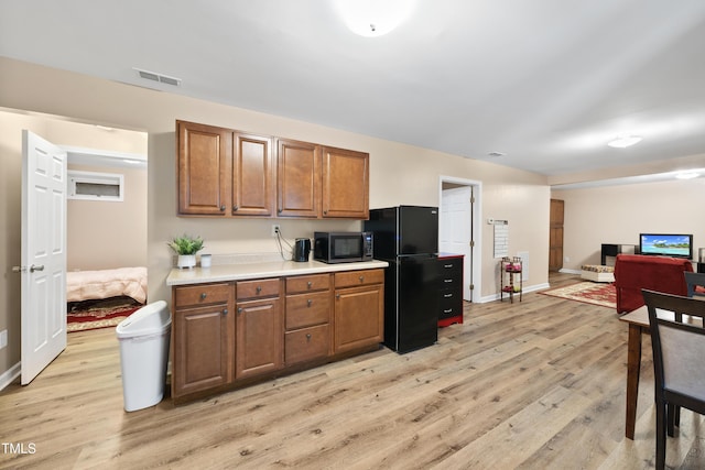 kitchen with visible vents, light wood-style flooring, stainless steel microwave, brown cabinets, and freestanding refrigerator