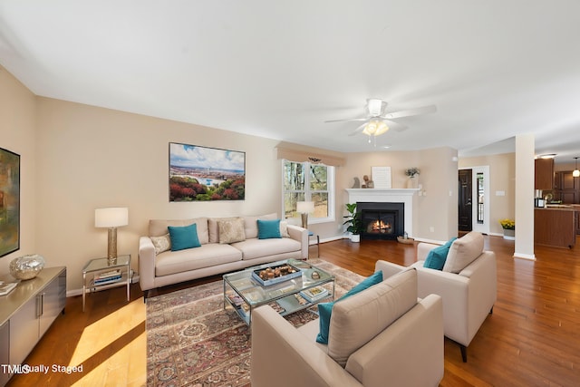 living room featuring ceiling fan, a glass covered fireplace, wood finished floors, and baseboards