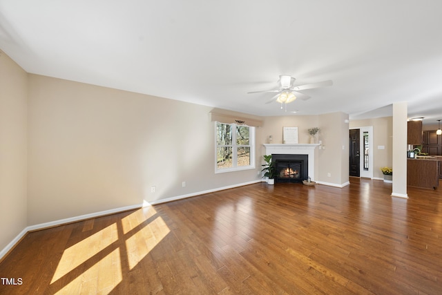 unfurnished living room featuring ceiling fan, a lit fireplace, dark wood-type flooring, and baseboards