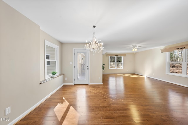 interior space featuring ceiling fan with notable chandelier, wood-type flooring, and baseboards