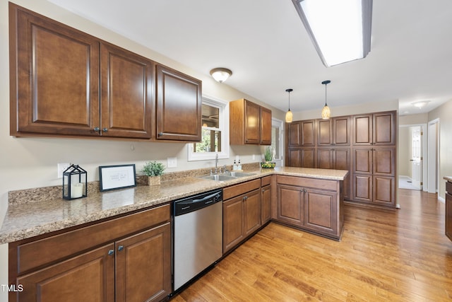 kitchen featuring a peninsula, a sink, dishwasher, light wood finished floors, and decorative light fixtures