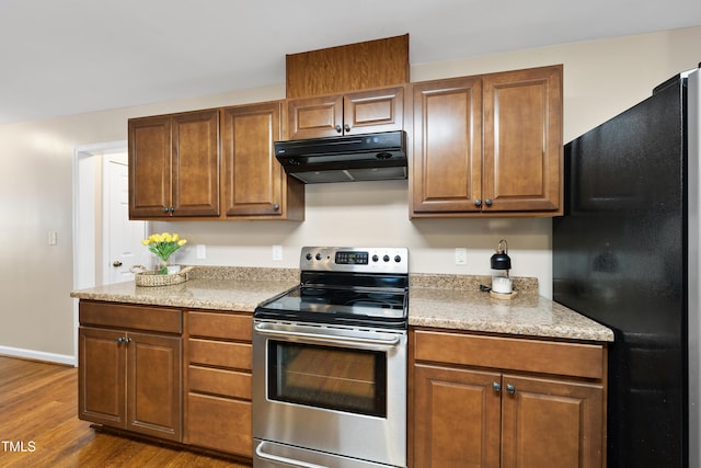 kitchen with electric range, brown cabinetry, freestanding refrigerator, wood finished floors, and under cabinet range hood