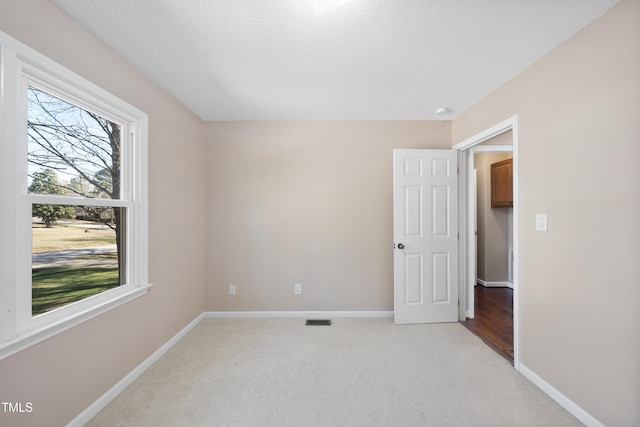 interior space with baseboards, visible vents, a textured ceiling, and light colored carpet