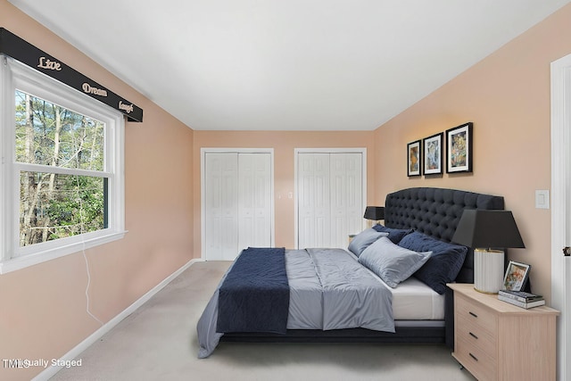 bedroom with light carpet, two closets, and baseboards