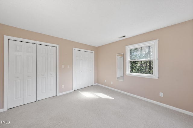 unfurnished bedroom with baseboards, carpet floors, visible vents, and multiple closets